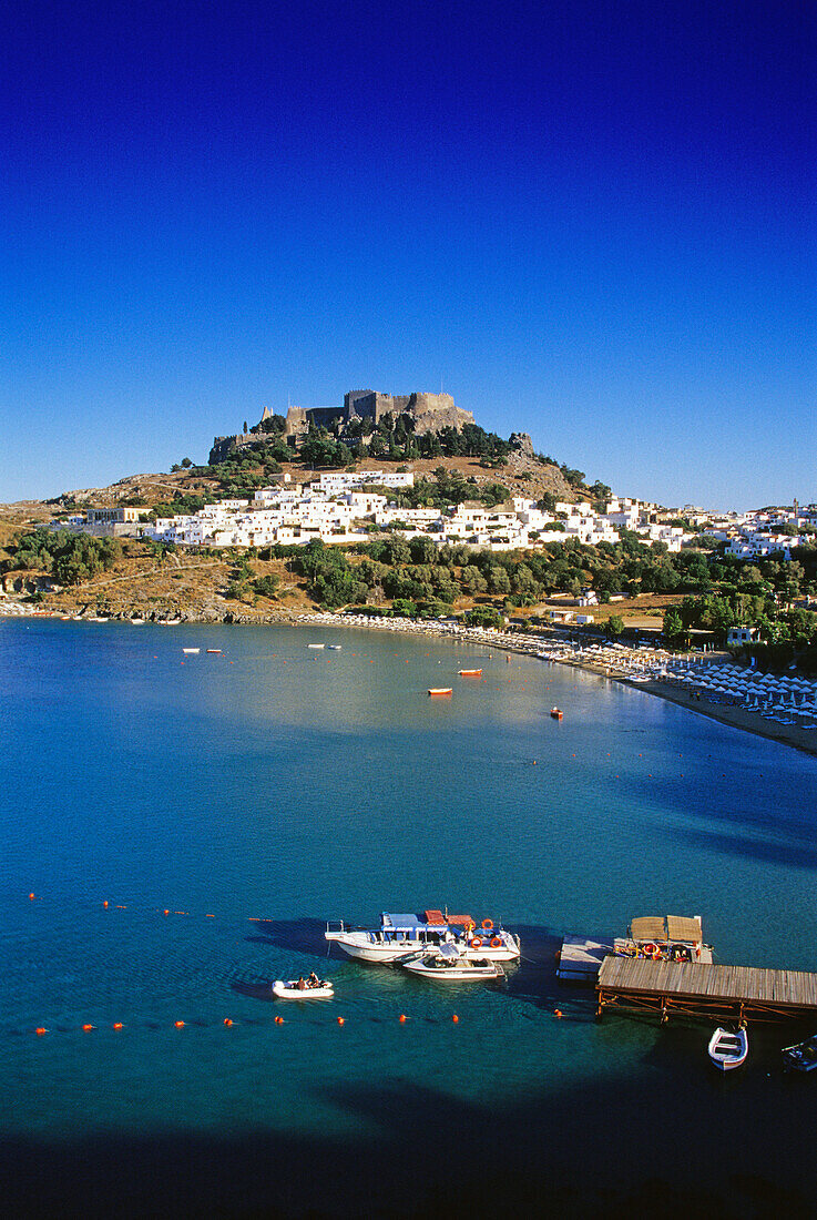 View at bay with beach, city and acropolis under blue sky, Lindos, Island of Rhodes, Greece, Europe