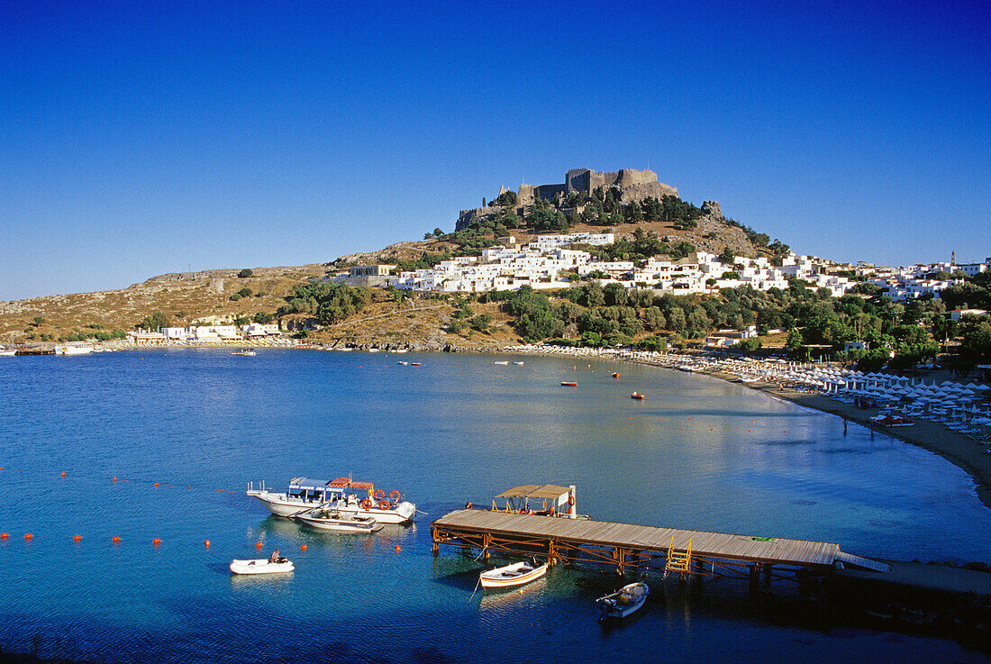 Blick auf die Bucht mit Strand und Akropolis unter blauem Himmel, Lindos, Rhodos, Griechenland, Europa