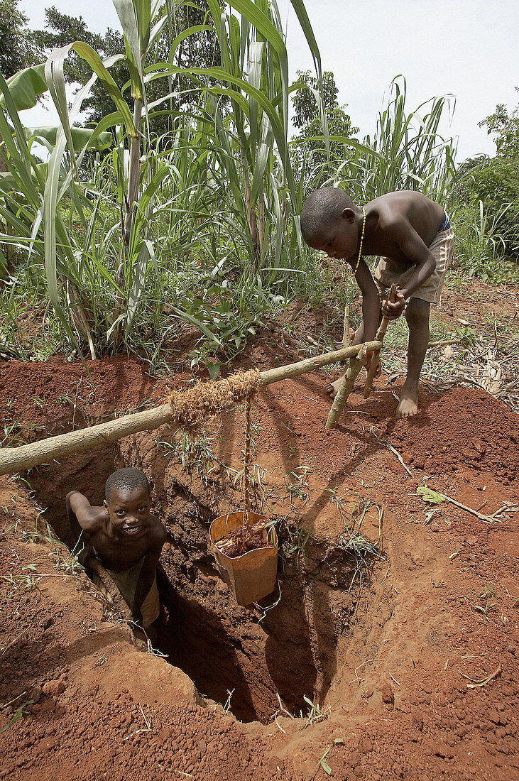 UGANDA  Boys digging a pit latrine, and hauling up the dirt with a winch and small bucket  Kayunga District