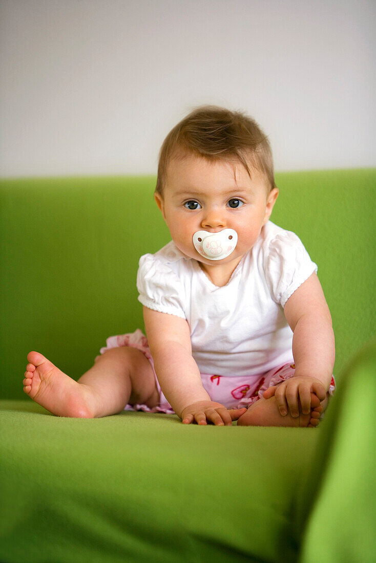 Baby (8 Monate) mit einem Schnuller blickt in die Kamera, Wien, Österreich