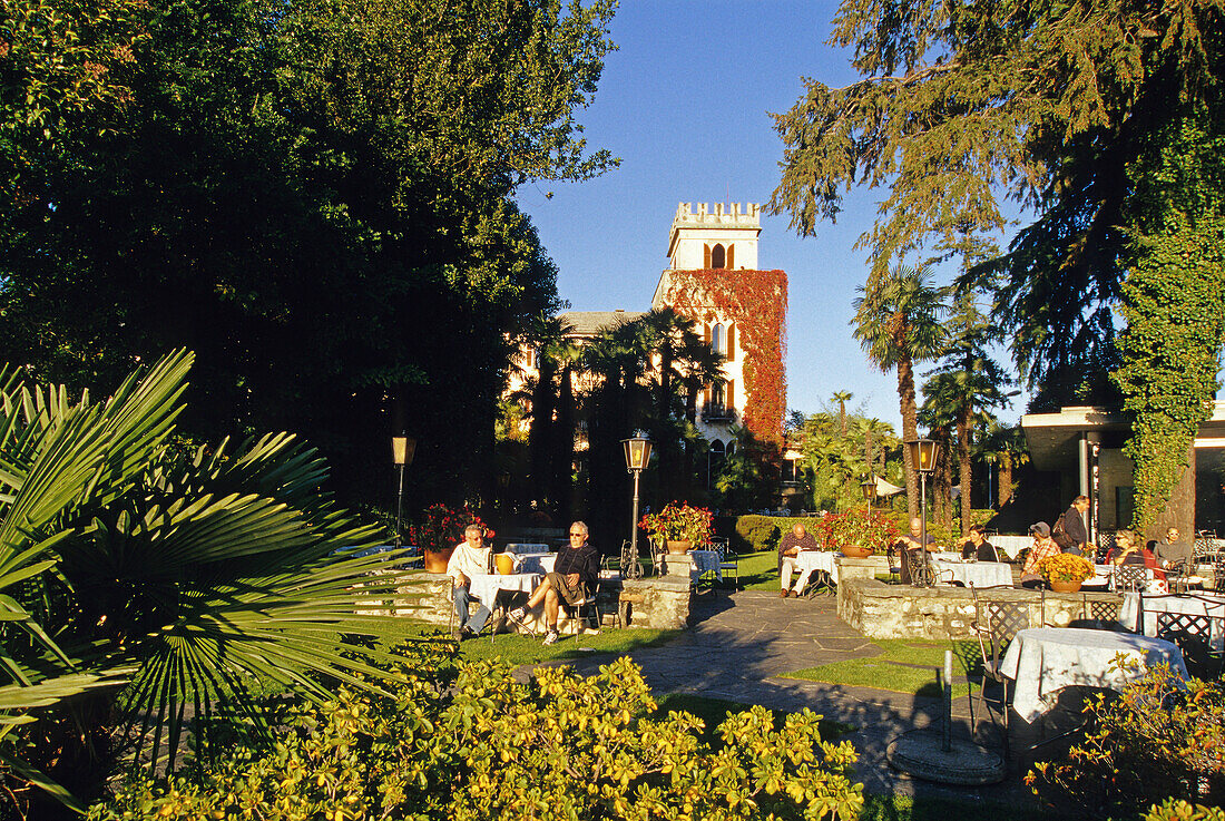 Menschen im Park vor dem Hotel Castello im Sonnenlicht, Ascona, Lago Maggiore, Tessin, Schweiz, Europa
