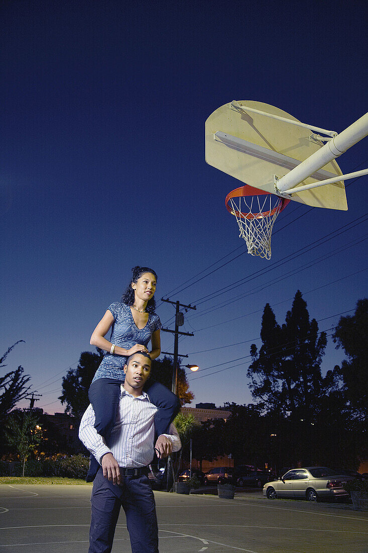 A young man gives a young woman a piggy back ride at a basketball court, Berkeley, California, USA
