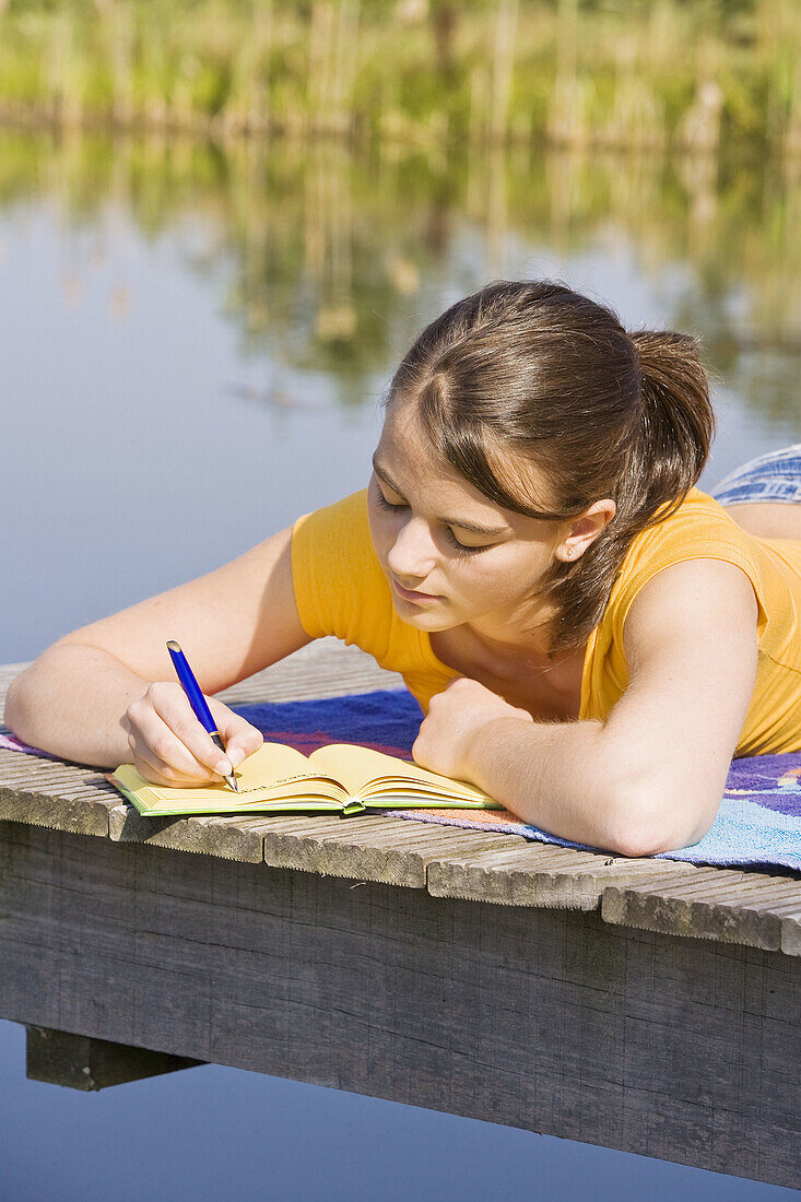 Young girl writing her diary at a lake