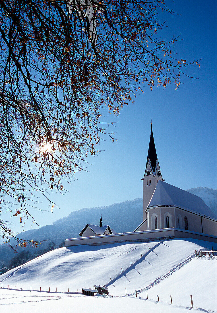 Kirche auf verschneitem Hügel im Sonnenlicht, Kreuth, Bayern, Deutschland, Europa