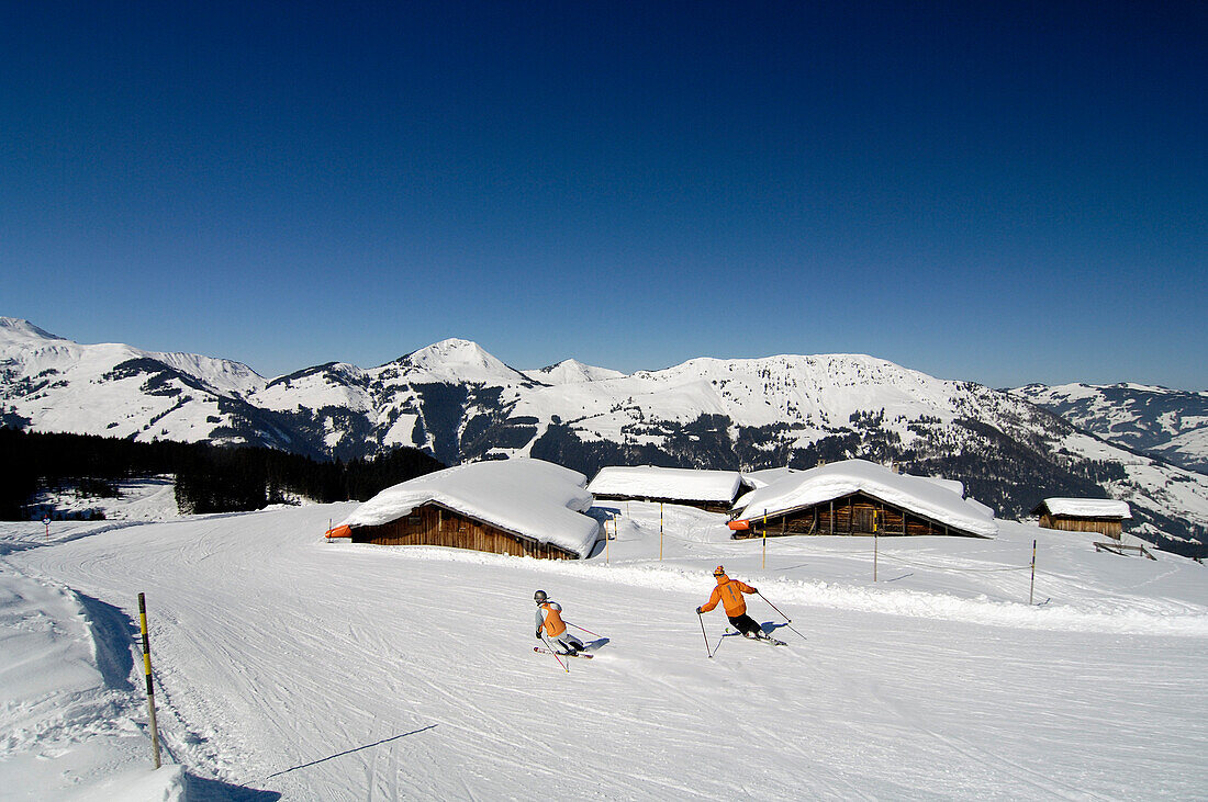 Skifahrer auf einer Skipiste unter blauem Himmel, Kitzbüheler Alpen, Tirol, Österreich, Europa