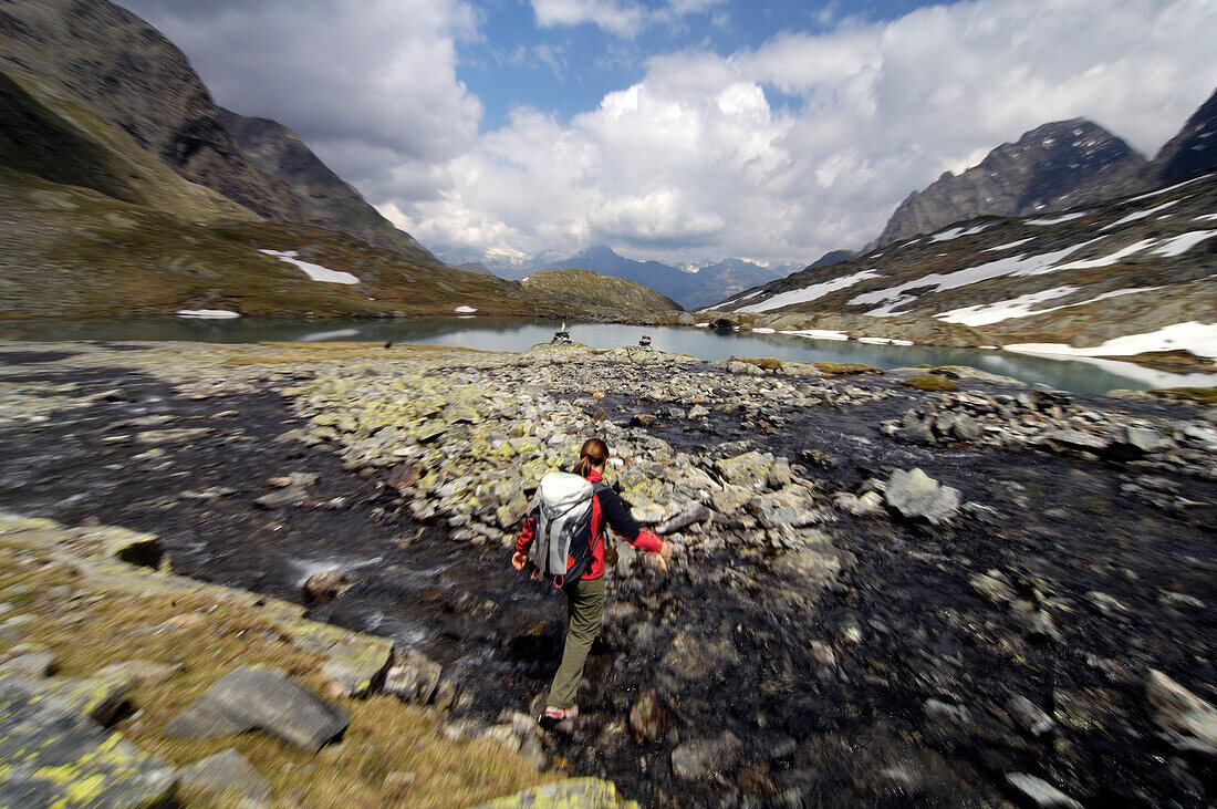 Woman with rucksack jumping over a mountain stream, Hohe Tauern, Austria, Europe