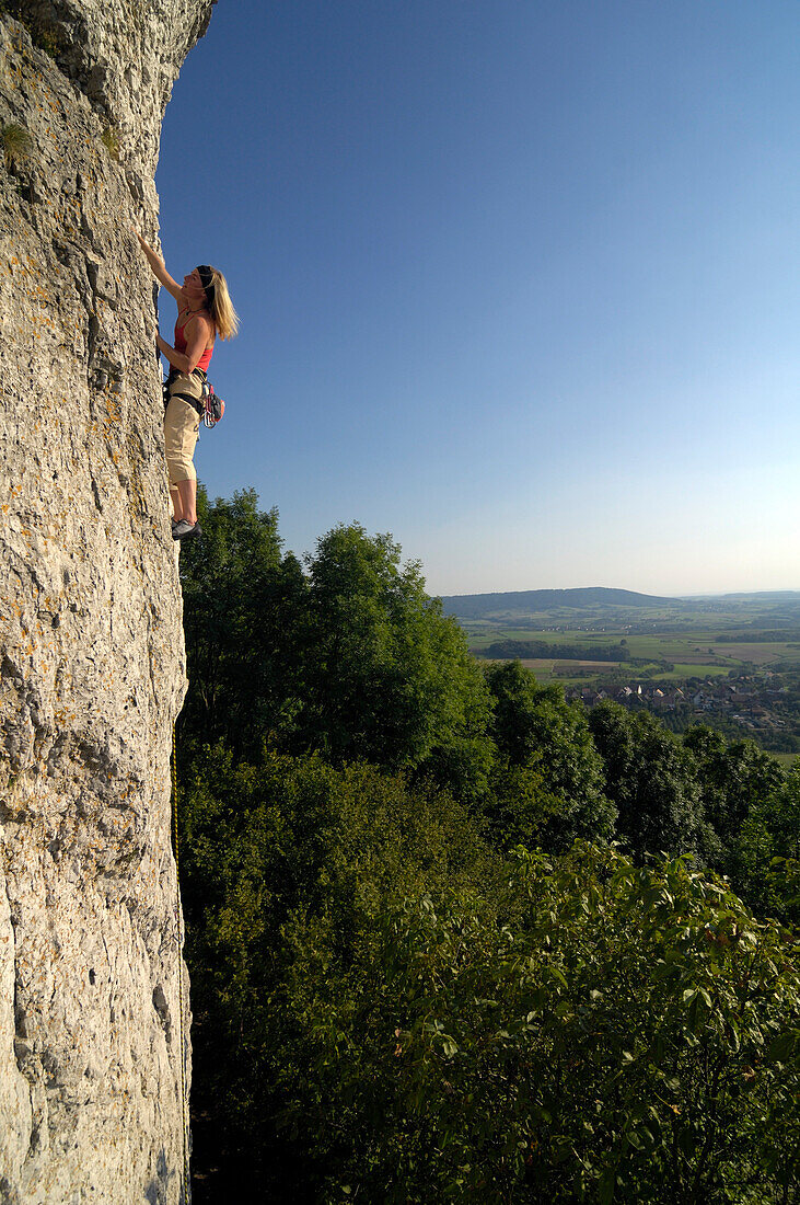 Woman climbing up a rock face in the sunlight, Franconian Switzerland, Bavaria, Germany, Europe