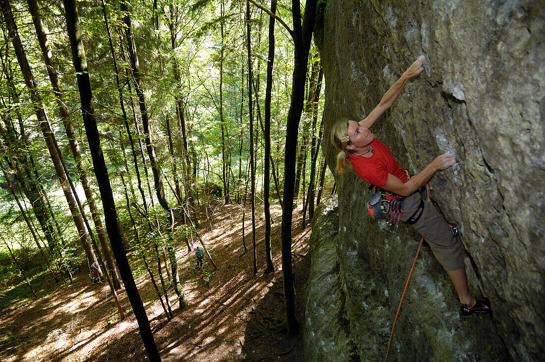 Frau klettert an einer Felswand im Wald, Fränkische Schweiz, Bayern, Deutschland, Europa