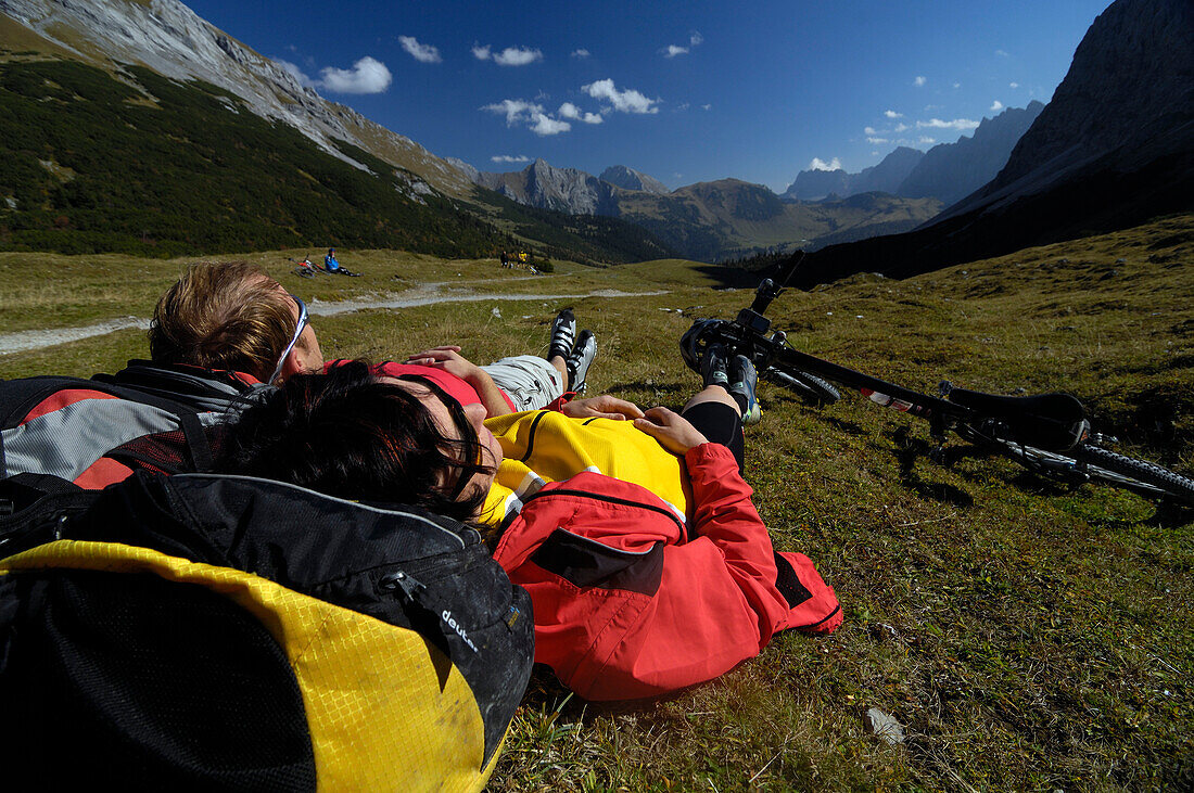 Couple lying on the grass having a rest, mountain bike tour in the Karwendel mountains, near Karwendelhaus, near Hinterriss, Tirol, Austria, Europe