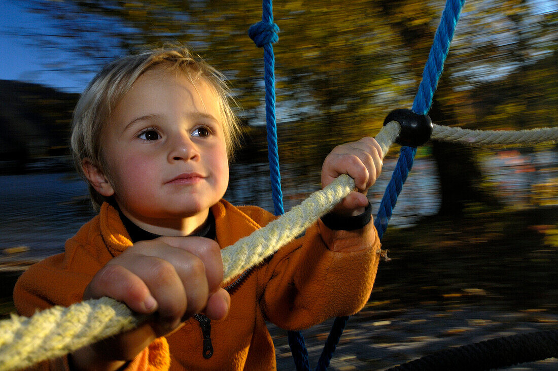 Kind auf dem Spielplatz, hält sich fest am Klettergerüst, Nahe Tegernsee, Oberbayern, Bayern, Deutschland, Europa