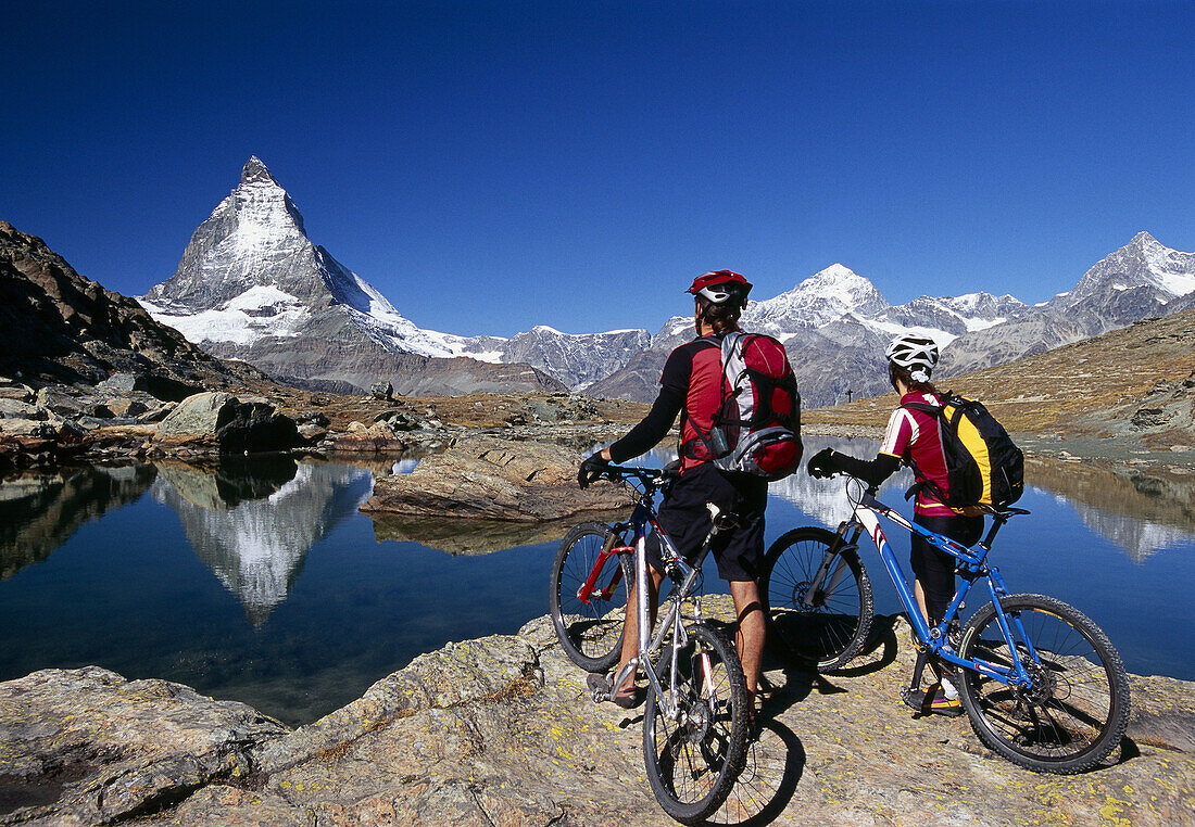 Couple with mountain bikes enjoying view to Matterhorn, Zermatt, Canton of Valais, Switzerland