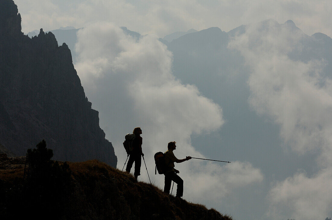 Hikers with hiking poles in front of overcast mountains, Rosengarten, Dolomites, South Tyrol, Italy, Europe