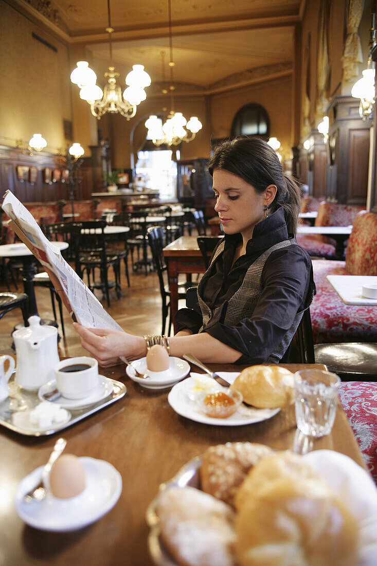 Frau mittleren Alters beim Frühstück in einem Café liest Zeitung, Wien, Österreich