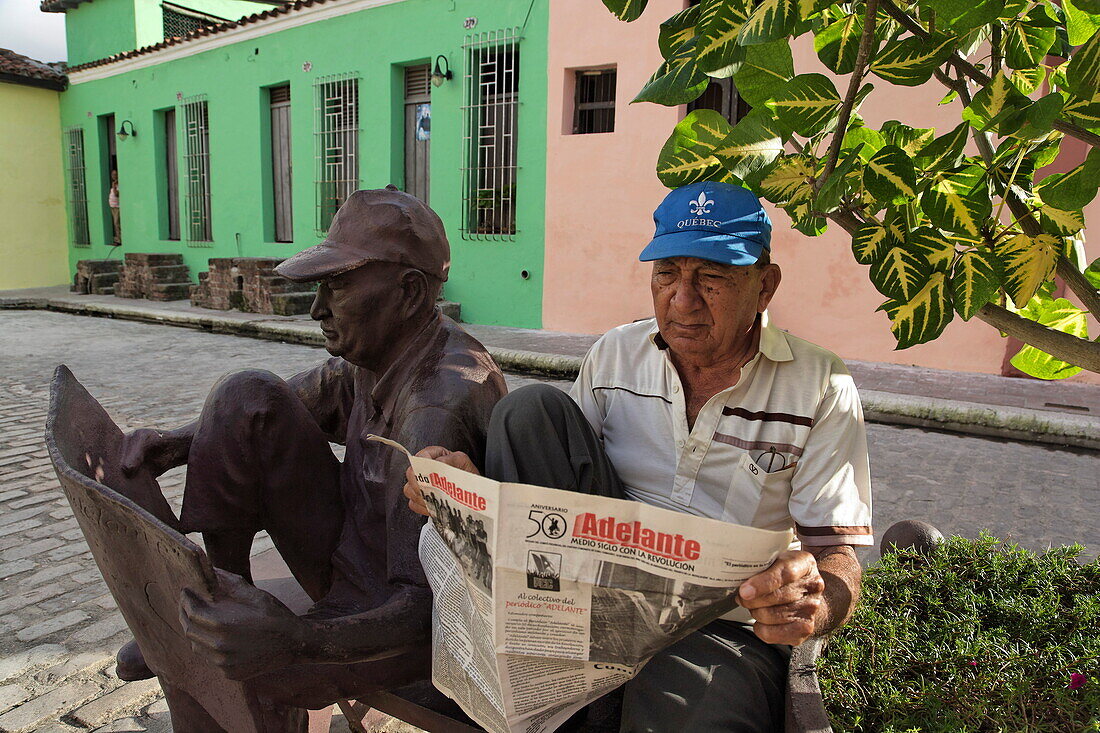 Man reading a newspaper next to a reading-man-sculpture, Plaza del Carmen, Camaguey, Camaguey, Cuba, West Indies