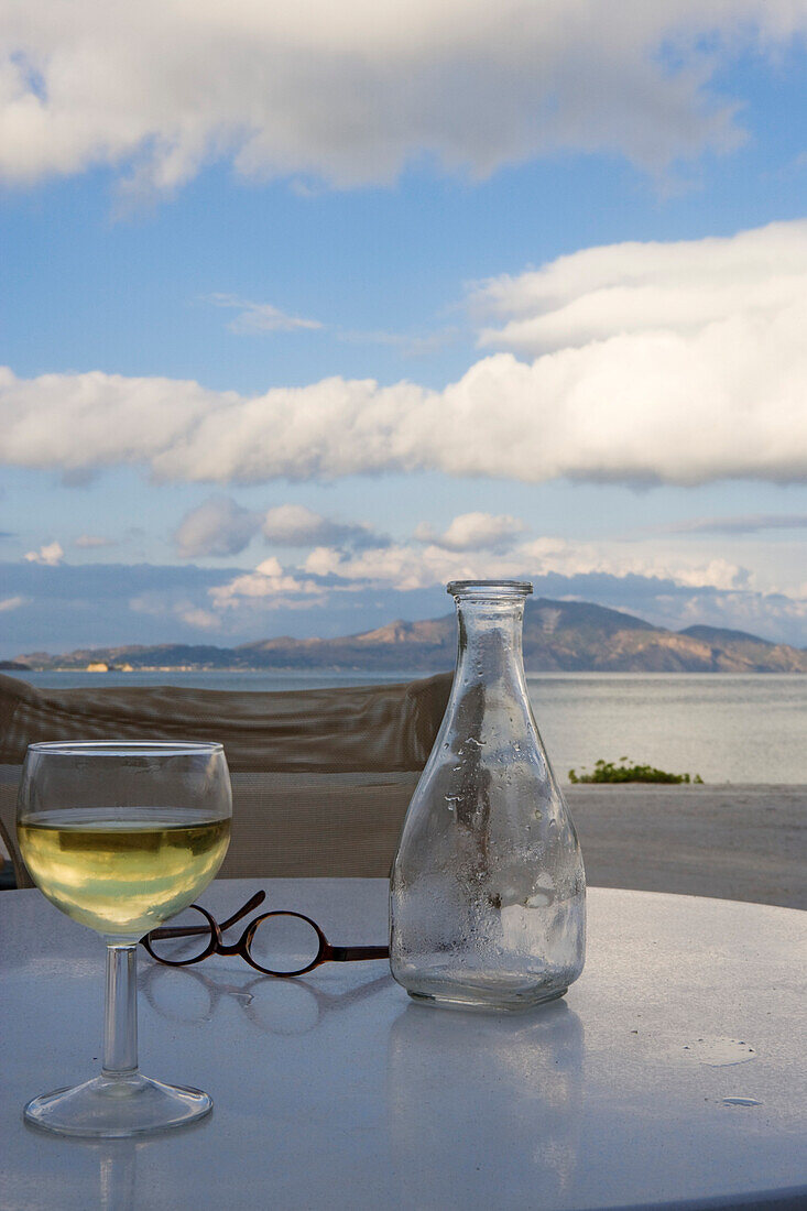 Blick über ein Weinglas und eine Karaffe auf Küstenlandschaft unter Wolkenhimmel, Limni Keriou, Zakynthos, Ionische Inseln, Griechenland, Europa