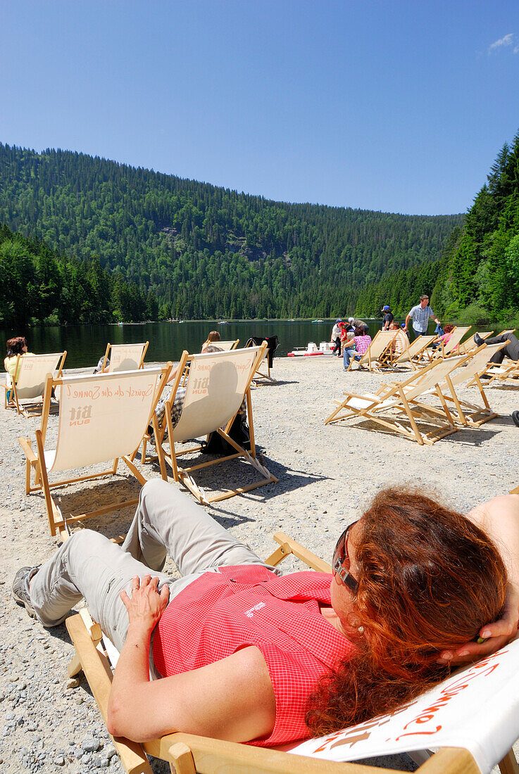 Woman sunbathing in beach chair, lake Grosser Arbersee, Bavarian Forest National Park, Lower Bavaria, Bavaria, Germany