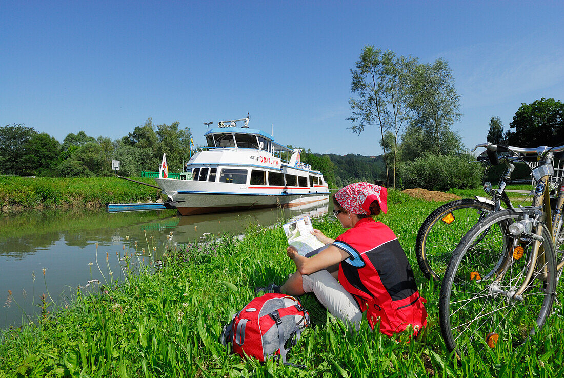 Woman sitting in meadow near river Danube while reading, Ardagger Markt, Lower Austria, Austria