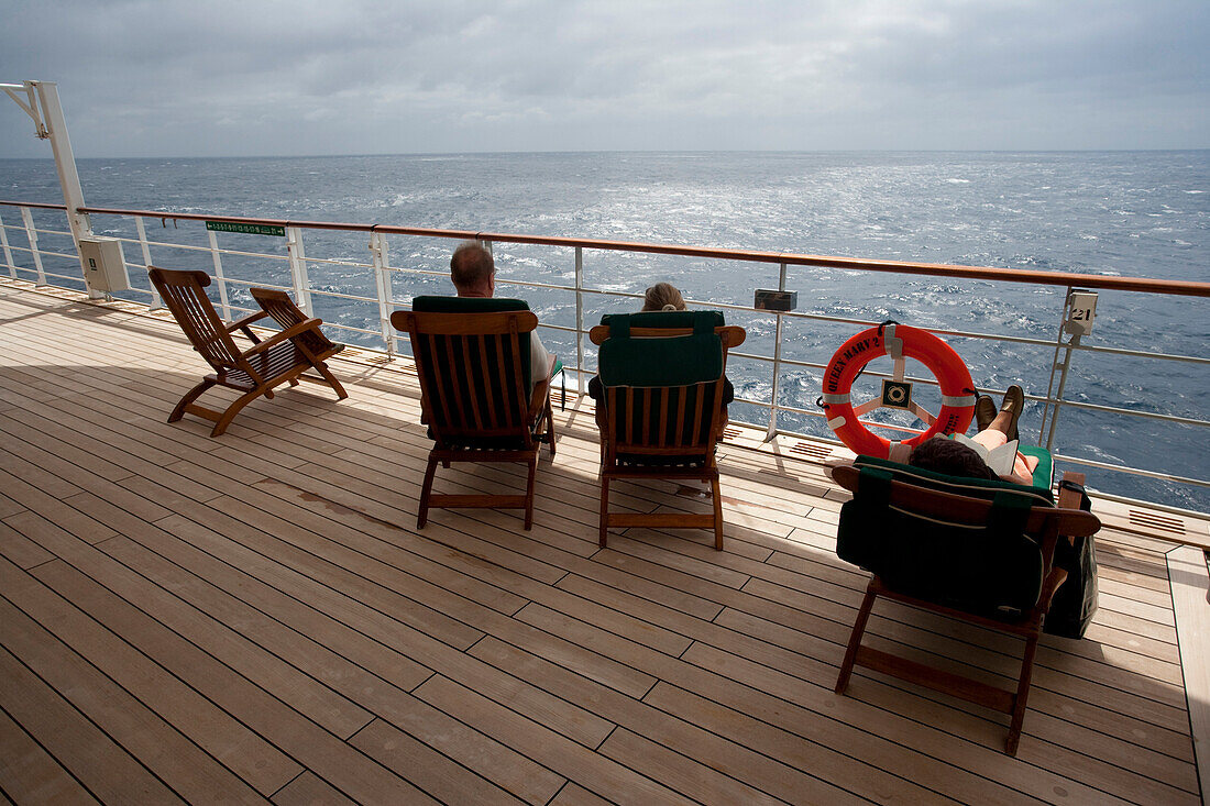 Passagiere sitzen im Liegestühlen, deck chairs auf dem Promenadendeck, Rettungsring, Kreuzfahrtschiff, Queen Mary 2, Nordatlantik, Atlantik