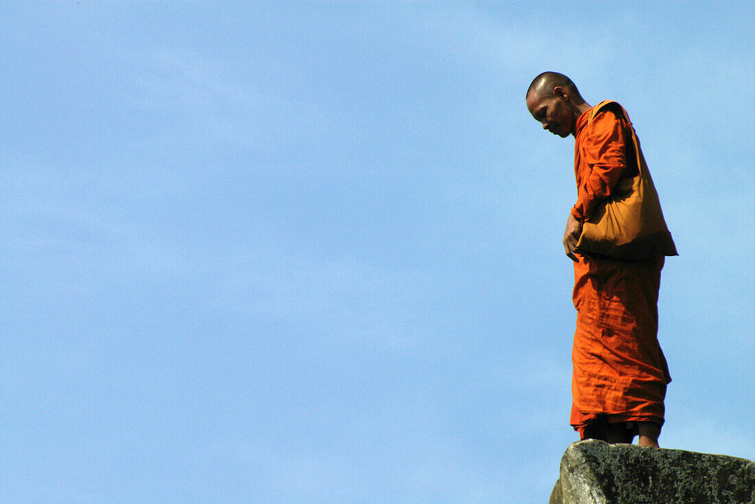 Monk at Angkor Wat in orange robe against blue sky, Siem Reap, near, Cambodia