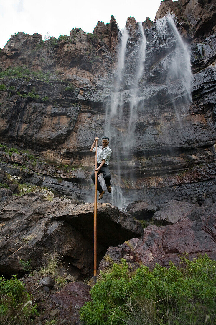 Mann springt mit kanarischem Hirtenstab vor dem Wasserfall Cascada el Escobar, Tal von El Risco, Parque Natural de Tamadaba, Gran Canaria, Kanarische Inseln, Spanien, Europa