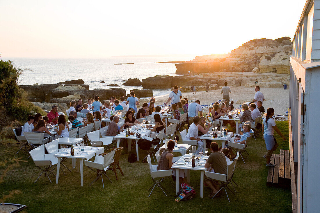 Tourists dining in a fish Restaurant on the beach at sunset, Praia do Evaristo, Albufeira, Algarve, Portugal