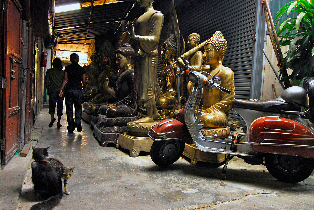 Devotional Shops, Buddhas sitting and standing on the pavement in a backstreet alley, Old Town with scooter and cats and people, Bamrung Muang, Bangkok, Thailand, Asia