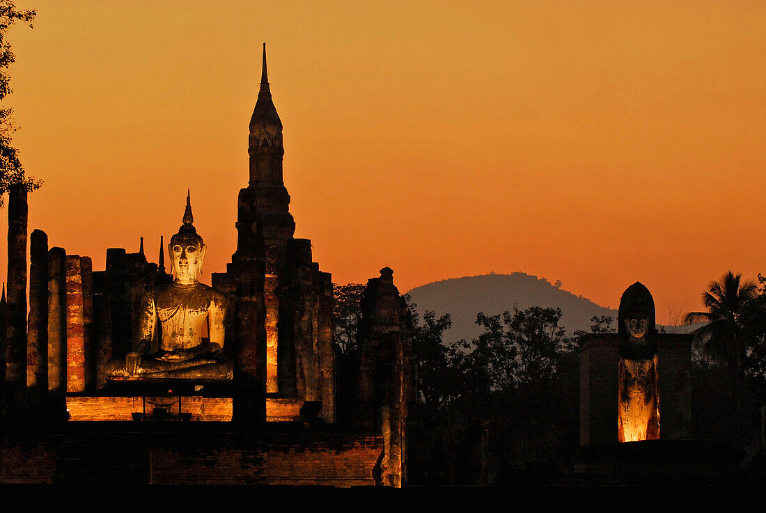 Illuminated Buddha in evening light with orange coloured sky at Wat Mahathat, Sukothai Historical Park, Central Thailand, Asia