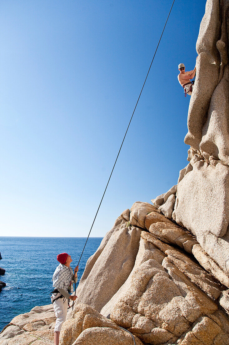 Climbers on a granitic rock on shore under blue sky, Capo Testa, Santa Teresa  Gallura, Sardinia, Italy, Europe