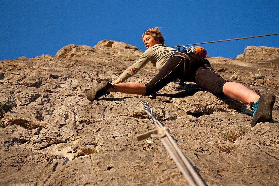 Junge Frau klettert an einer sonnenbeschienenen Felswand hoch, Jerzu, Sardinien, Italien, Europa