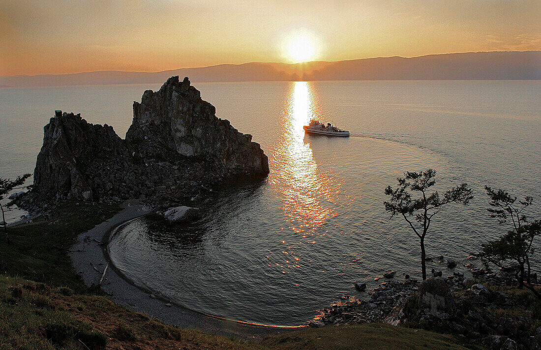 Boat near Shaman Rock at Cape Burchon on Olchon Island at sunset, Lake Baikal, Russian Federation