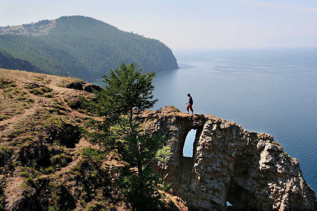 View at Cape Choboi on Olchon Island with man crossing rock window, Lake Baikal, Russian Federation