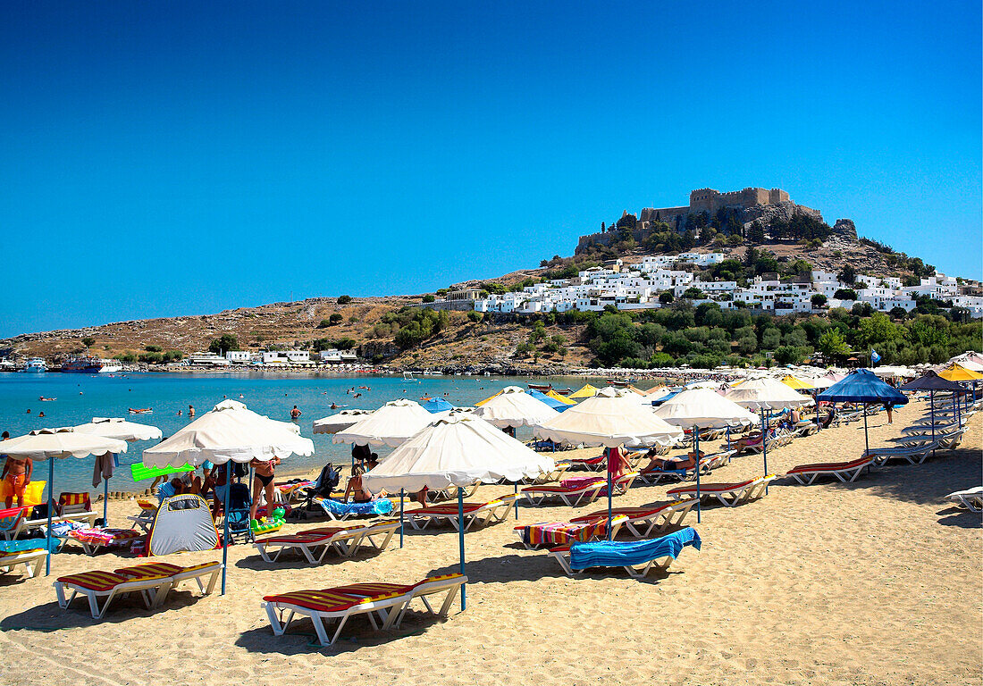 Beach scene with view of Lindos town and hilltop acropolis, Lindos, Rhodes Island, Greek Islands