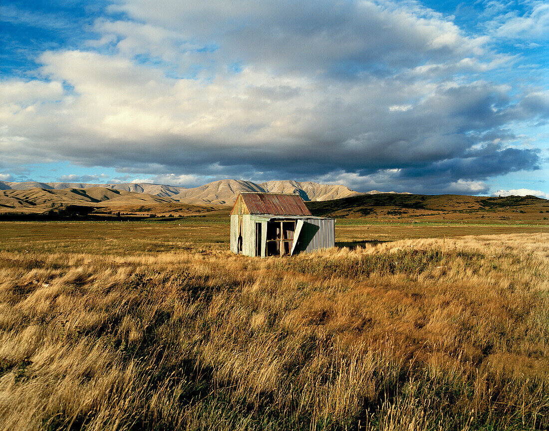 Weideland mit kleiner Hütte unter Wolkenhimmel, Central Otago, Südinsel, Neuseeland