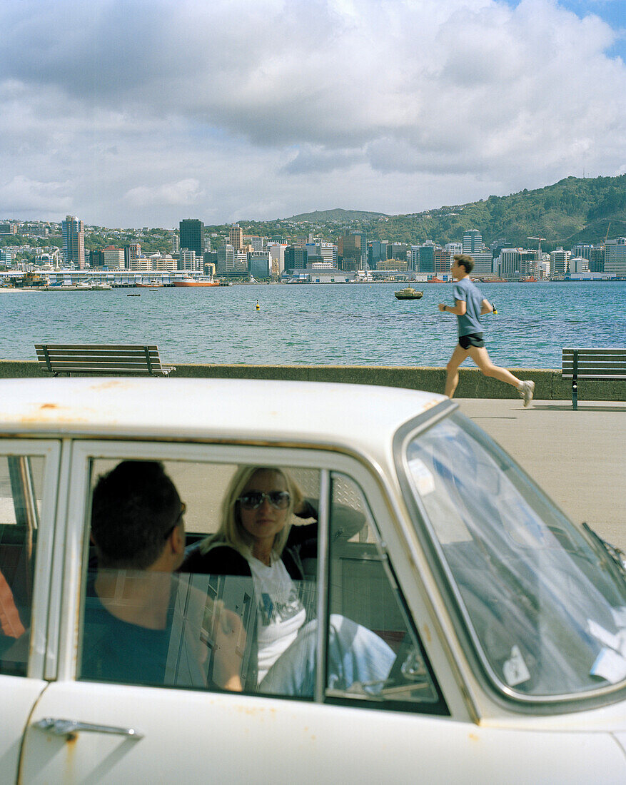 Ein Paar in einem Auto und ein Jogger auf der Hafenpromenade, Oriental Parade, Wellington, Nordinsel, Neuseeland