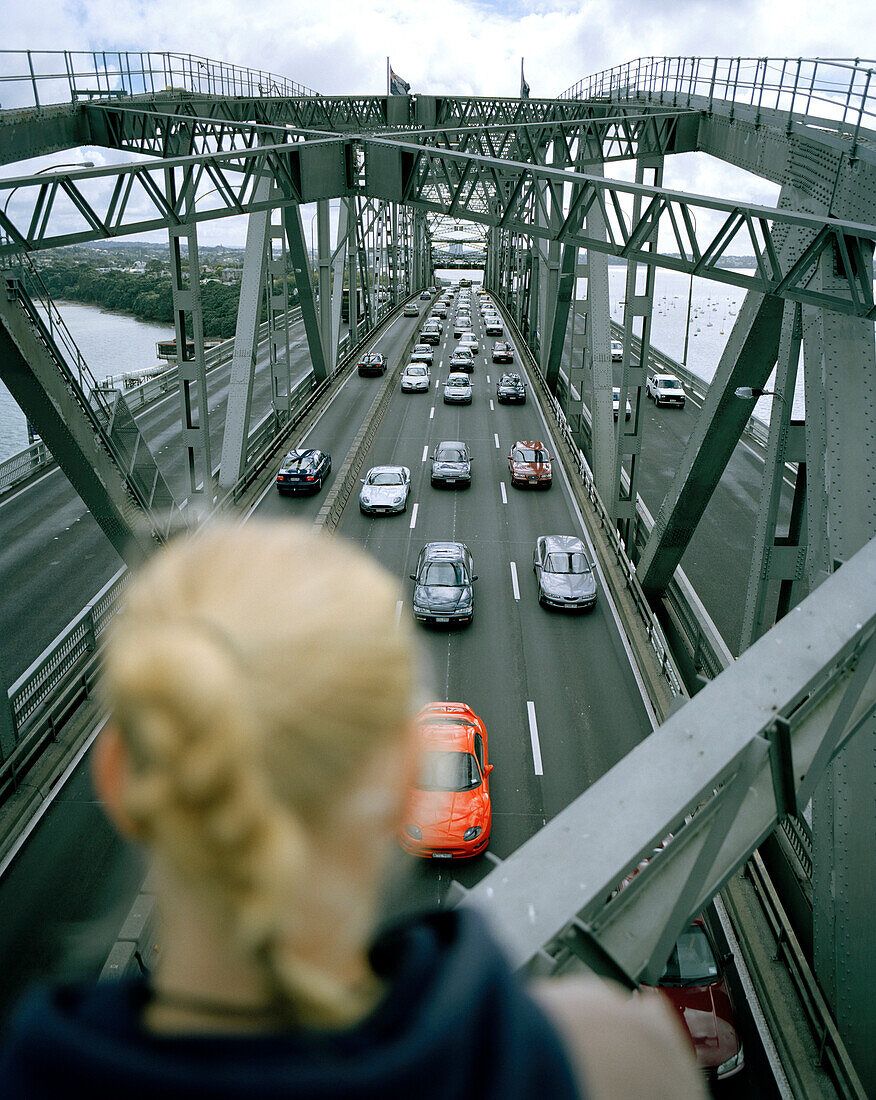Junge Frau auf den Stahlbögen der Harbour Bridge schaut auf Autos auf dem Highway 1, Auckland, Nordinsel, Neuseeland