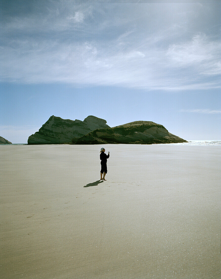 Frau auf weitem Sandstrand bei Ebbe, Wharariki Beach, Nordküste, Südinsel, Neuseeland