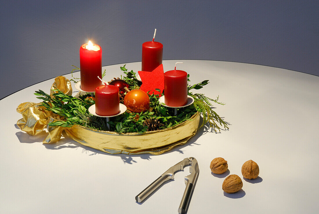 Adventskranz mit einer brennenden Kerze, mit Nussknacker und Walnüssen im Vordergrund