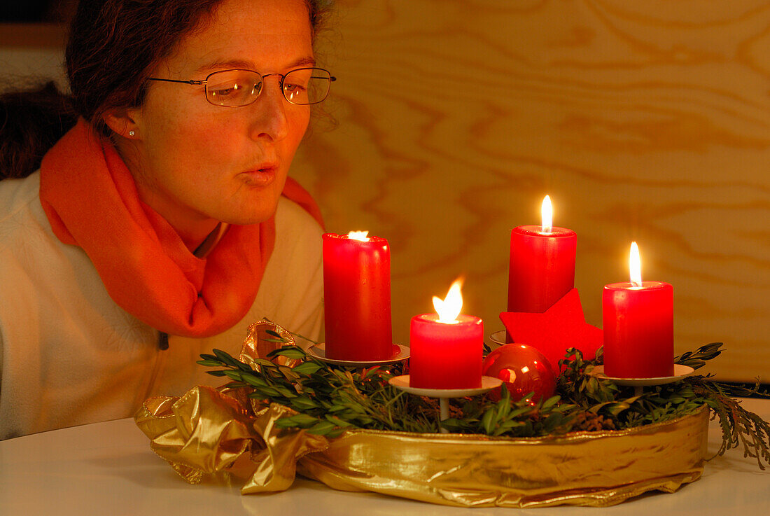 Woman blowing out four candles at advent wreath