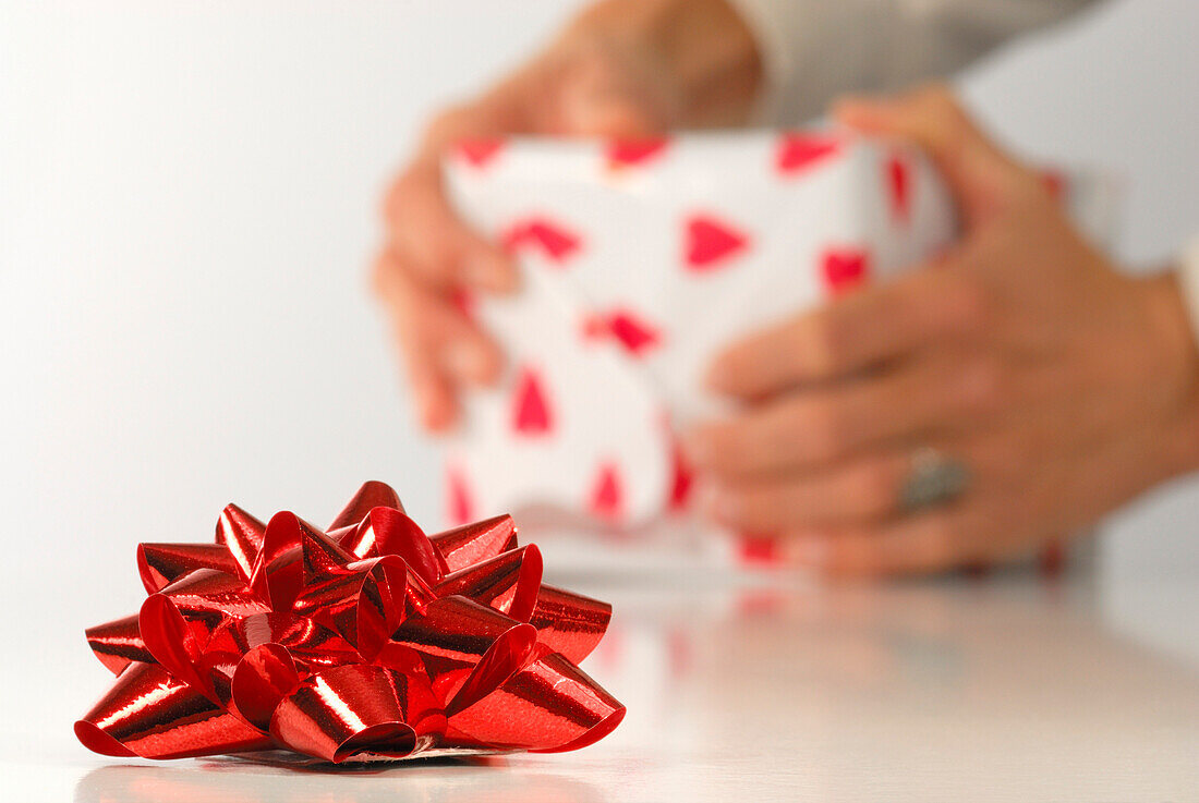 Rote Geschenkschleife mit Person im Hintergrund, die Geschenk einpackt