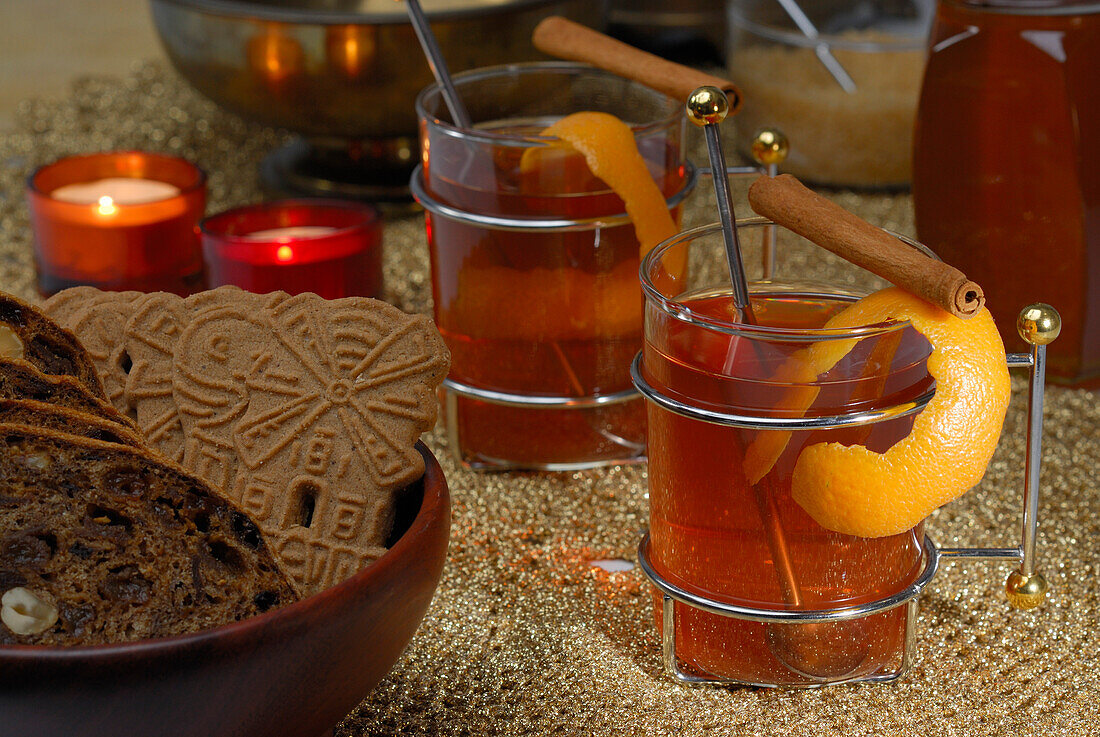 Zwei Teegläser mit Orangenschale und Zimtstange dekoriert und Schale mit Weihnachtsgebäck