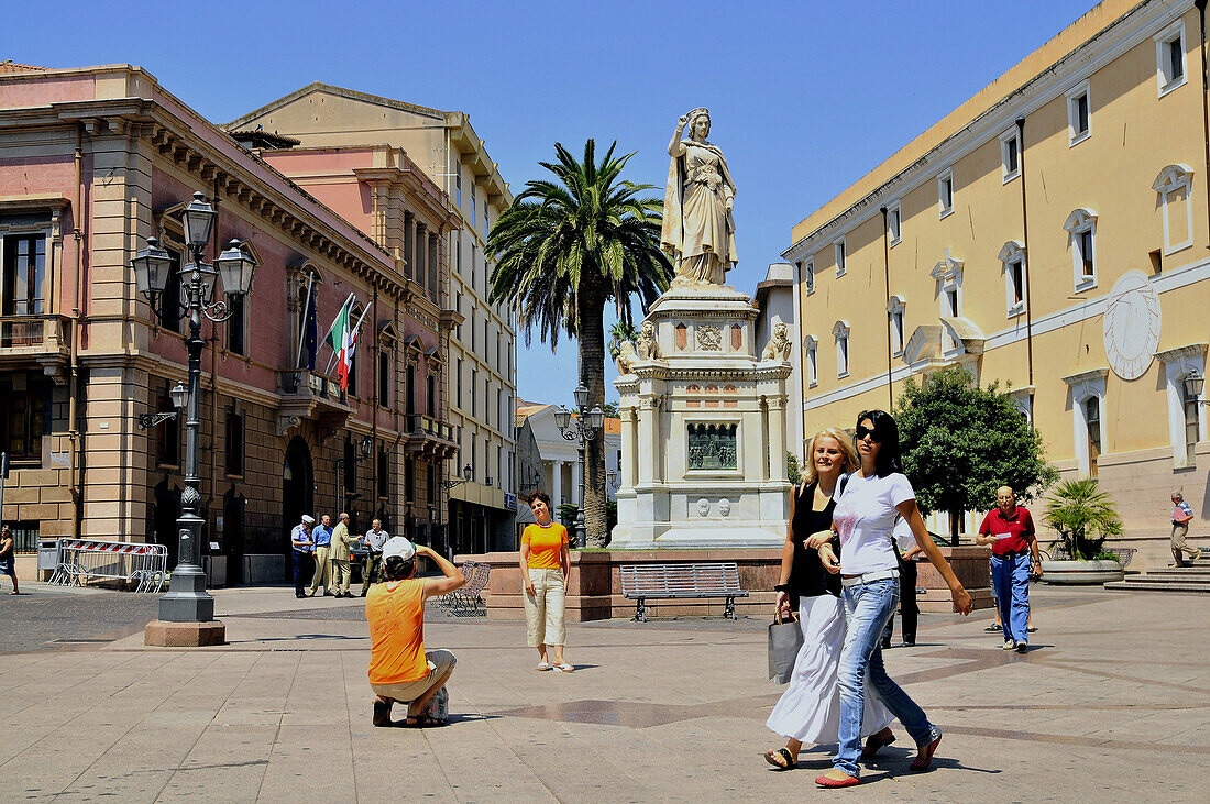 A monument and people on the sunlit Piazza Eleonora, Oristano, Sardinia, Italy, Europe