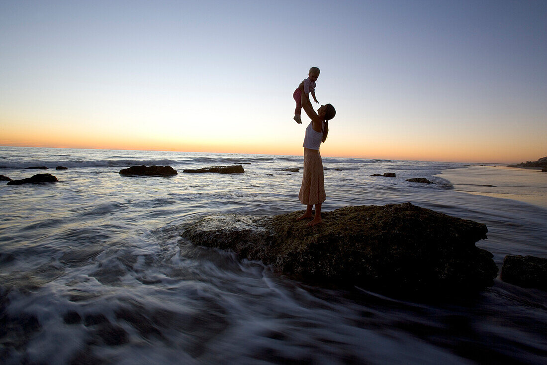 Mother and child on a rock on the waterfront at sunset, Punta Conejo, Baja California Sur, Mexico, America