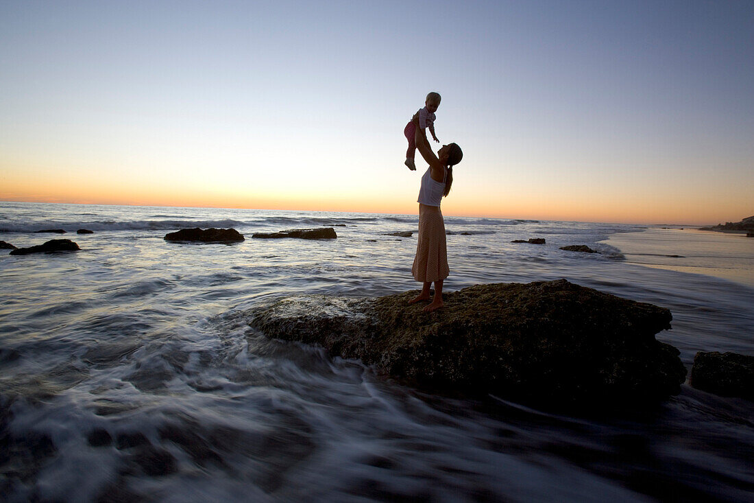 Mutter und Kind auf einem Felsen am Meer bei Sonnenuntergang, Punta Conejo, Baja California Sur, Mexiko, Amerika