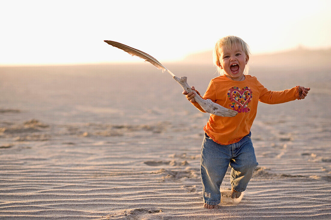 Little girl running with a feather in her hand over the sandy beach, Punta Conejo, Baja California Sur, Mexico, America