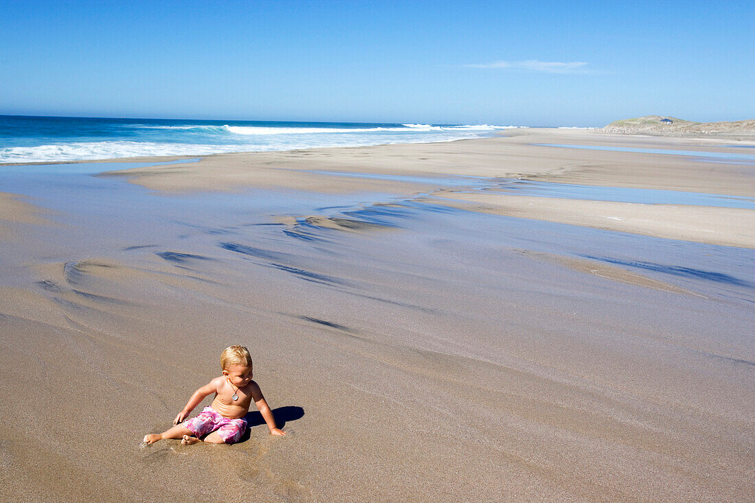 Kleines Mädchen sitzt am Strand im Sonnenlicht, Punta Conejo, Baja California Sur, Mexiko, Amerika