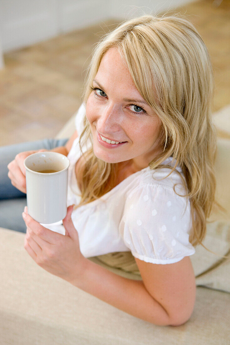 Adult, Adults, At home, Beverage, Beverages, Blonde, Blondes, Blue eyed, Blue eyes, Blue-eyed, Caucasian, Caucasians, Coffee, Color, Colour, Contemporary, Couch, Couches, Cup, Cups, Drink, Drinks, Facing camera, Fair-haired, Female, From above, grin, grin