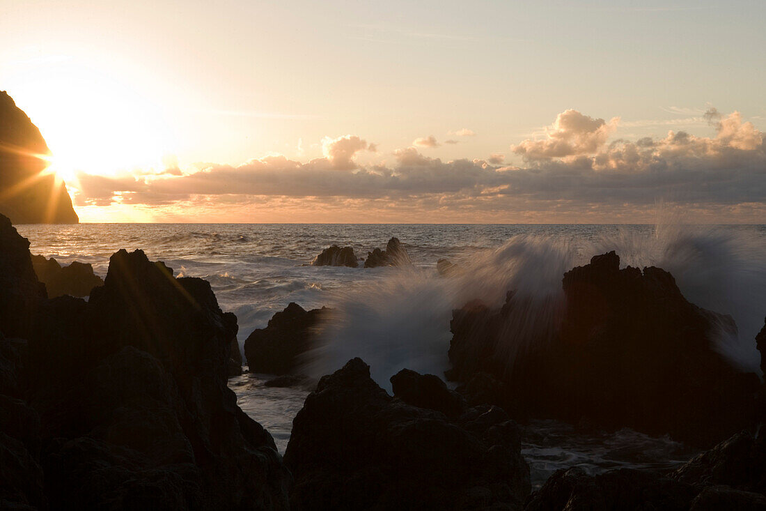 Wellen brechen an Felsen aus Lavastein bei Sonnenuntergang, Porto Moniz, Madeira, Portugal