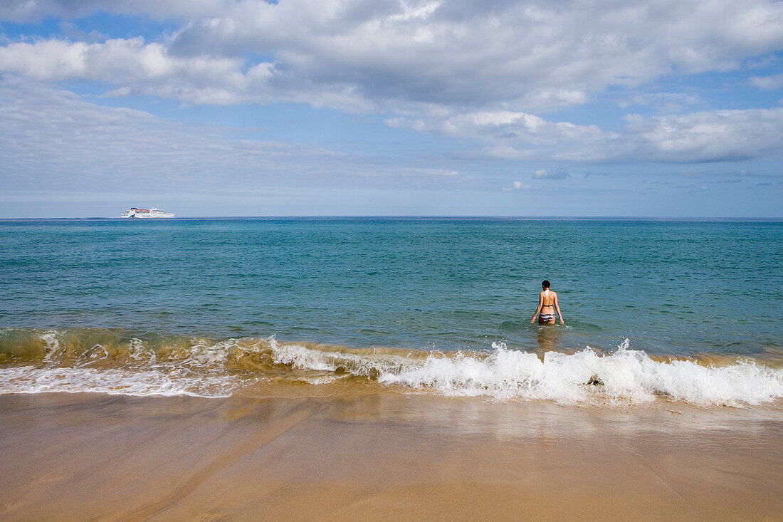 Woman going for a swim on Porto Santo Beach with Porto Santo Line Ferry Lobo Marinho on the horizon, Porto Santo, near Madeira, Portugal