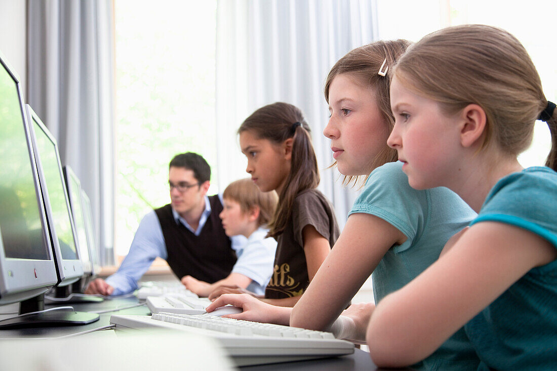 Male teacher helping pupils in computer room, Hamburg, Germany