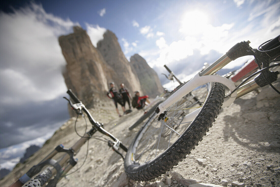 Three persons resting, mountain bikes in foreground, Tre Cime di Lavaredo, Veneto, Italy